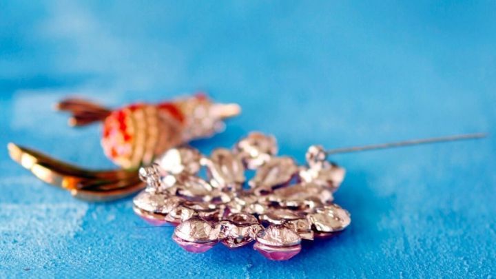 Eine glitzernde Brosche liegt auf einem blauen Hintergrund, wobei die Nadel des Schmuckst&uuml;cks hervorragt.
