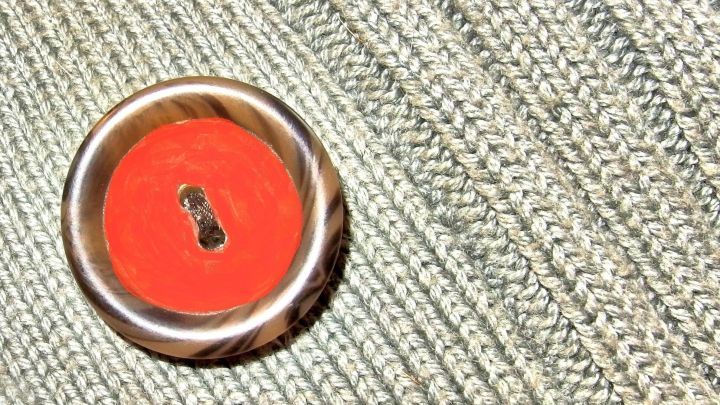 Ein gro&szlig;er roter Knopf liegt auf einem gestreiften, grauen Stoff, der ihm Kontrast und visuelle Spannung verleiht.