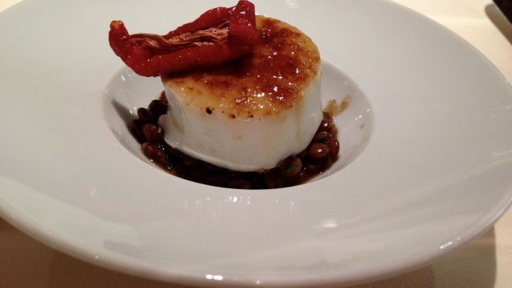 Eine Pannacotta mit einer karamellisierten Oberfl&auml;che und einem roten Topping ruht elegant in einer wei&szlig;en Sch&uuml;ssel.