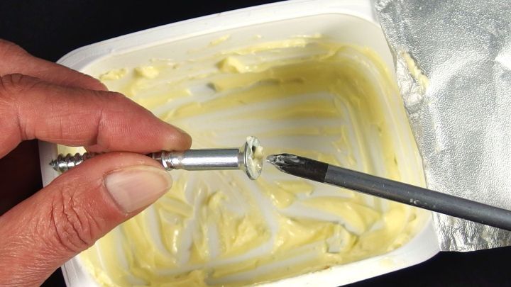 Ein Schraubendreher wird benutzt, um eine Schraube zu l&ouml;sen, w&auml;hrend sie in einer Margarine-Packung steckt.