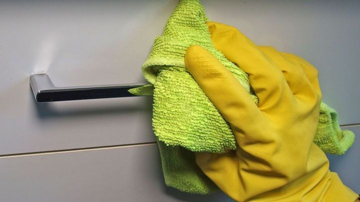 Eine gelbe Hand mit einem Mikrofasertuch reinigt einen T&uuml;rgriff in einer sauberen Wohnumgebung.