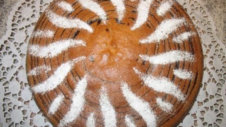 Eine runde Quark-Zebra-Torte liegt auf einem Spitzendeckchen, mit gezuckerten Streifenmuster wie Zebrafell dekoriert.