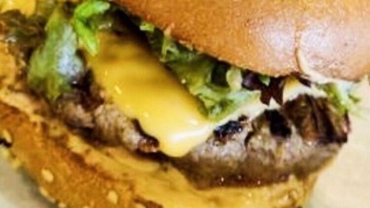 Ein saftiger Abi-Burger mit Sesam-Br&ouml;tchen, geschmolzenem K&auml;se und frischem Gem&uuml;se liegt appetitlich auf einem Teller.