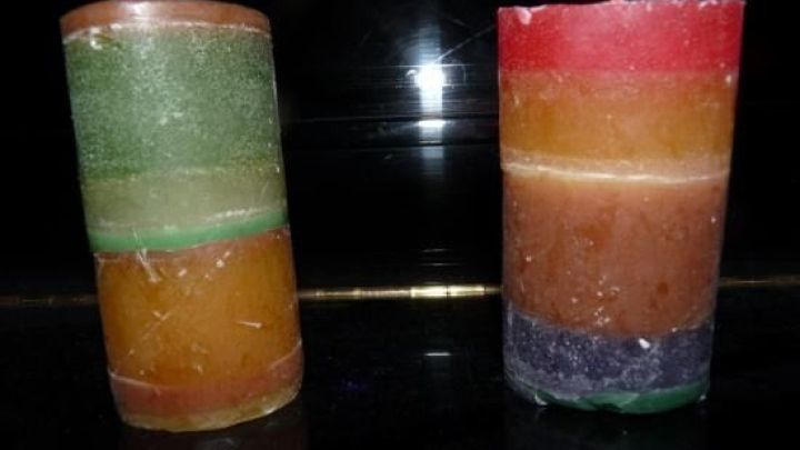 Bunte Kerzen aus Toilettenpapierrollen stehen nebeneinander, jede in verschiedenen Farben, auf einem dunklen Hintergrund.