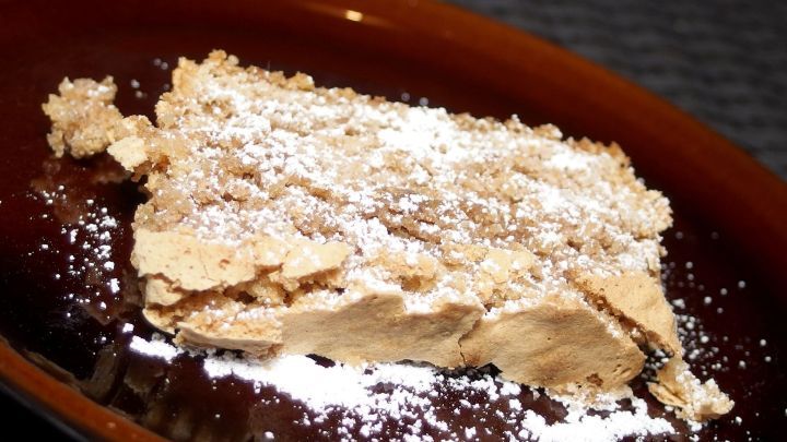 Der Nusskuchen aus Kastenform liegt auf einem dunkelbraunen Teller, mit Puderzucker best&auml;ubt, vor einem grauen Hintergrund.