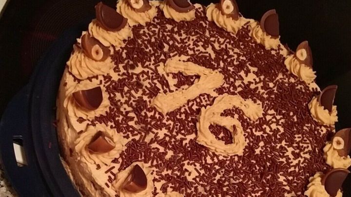 Eine runde Nuss-Karamell-Torte liegt auf einer dunklen Platte, mit einer dekorativen Verzierung und der Zahl 76 darauf.