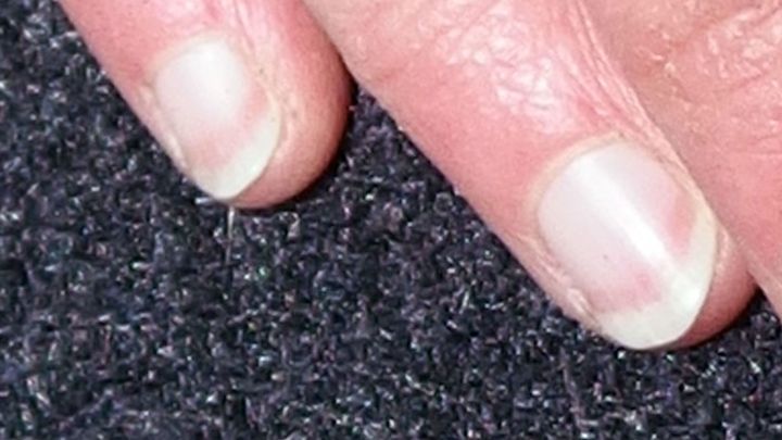 Wei&szlig;e Nagelspitzen liegen auf einer dunklen Oberfl&auml;che, wobei die Hand eine ruhige und pflegliche Position einnimmt.