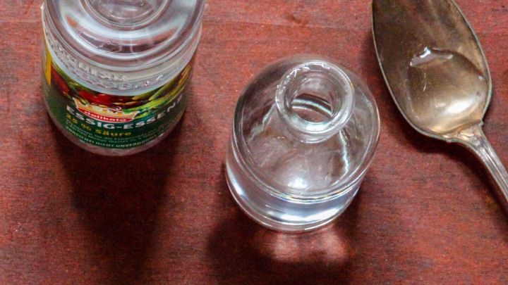 Eine Flasche Essig und ein kleines Glas stehen neben einem L&ouml;ffel auf einem Holzuntergrund, bereit zum Gurgeln gegen Halsschmerzen.