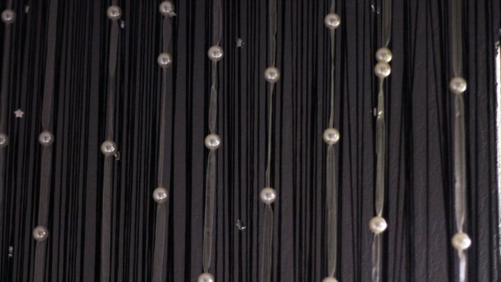 Fadenvorh&auml;nge h&auml;ngen an einer Wand, w&auml;hrend sie mit eleganten Perlen verziert sind, die sie hervorheben.