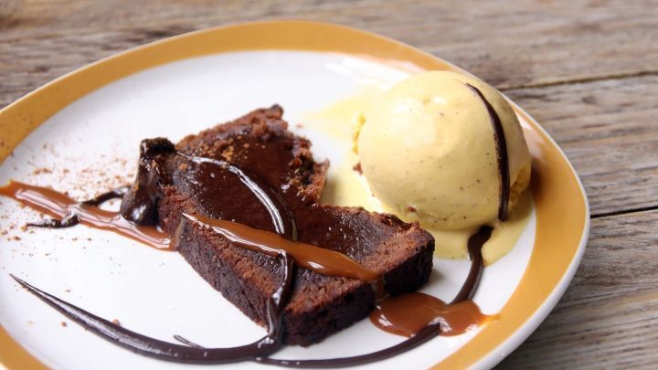 Ein St&uuml;ck saftiger Schokokuchen liegt auf einem Teller neben einer Kugel Vanilleeis und Schokoladensauce.