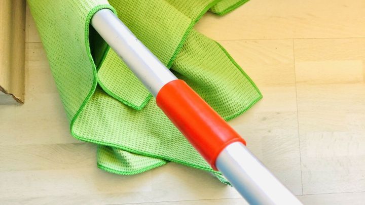 Ein gr&uuml;nes Tuch ist an einem Besenstiel befestigt, bereit zum Reinigen von Bodenecken in einem hellen Innenraum.