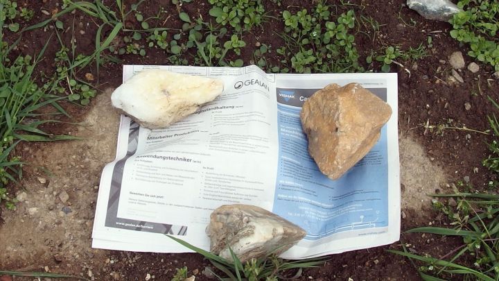 Ein auf dem Boden liegendes Papier, das mit Steinen beschwert ist, um Unkraut zu entfernen, umgeben von gr&uuml;nem Gras.