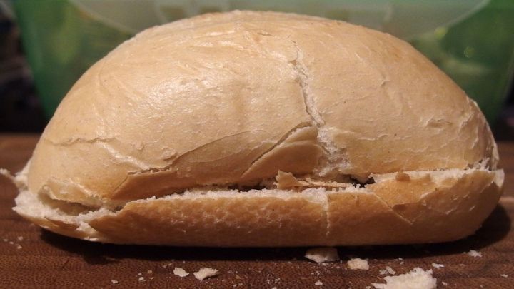 Ein ungebackenes Br&ouml;tchen liegt auf einem Holzbrett, mit einer tiefen Einschnittstelle f&uuml;r gleichm&auml;&szlig;iges Aufbacken.