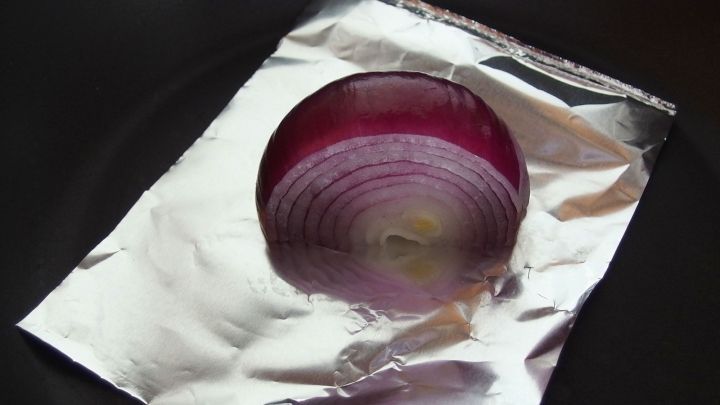 Eine rote Zwiebel liegt auf Alufolie in einer Pfanne, bereit zum Br&auml;unen in der Hitze des Kochprozesses.