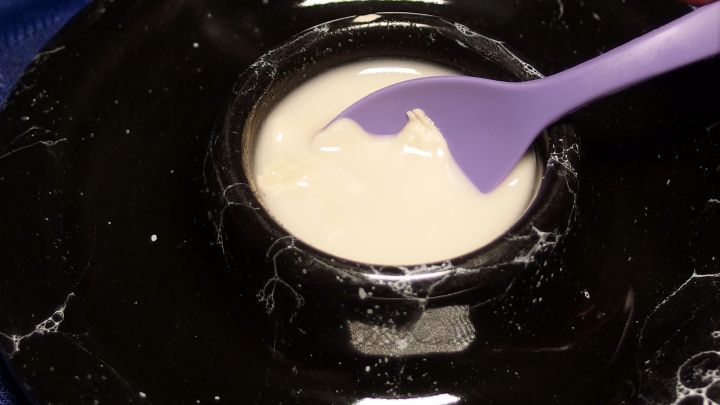 Eine lila Spachtel r&uuml;hrt eine cremige Substanz in einer schwarzen Schale. Diese wird m&ouml;glicherweise gegen Aphten im Mund eingesetzt.