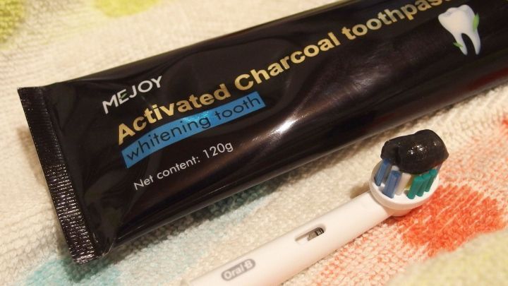 Eine Tube Aktivkohle-Zahnpasta liegt neben einer Zahnb&uuml;rste auf einem bunten Handtuch, bereit zur Anwendung f&uuml;r sch&ouml;ne wei&szlig;e Z&auml;hne.