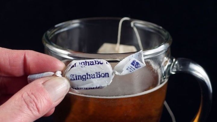 Eine Hand h&auml;lt einen Teebeutel &uuml;ber eine Tasse mit Ingwertee, die in einem dunklen Raum steht und dampft.