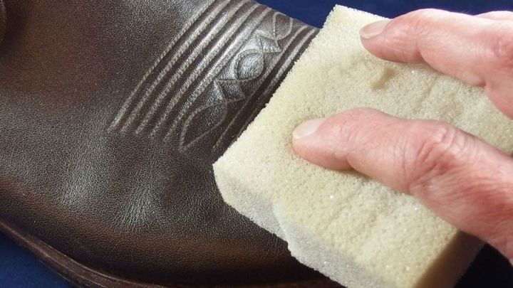 Ein handgehaltener Schaumstoffschaum reinigt einen Schuh, der auf einer dunklen Oberfl&auml;che liegt, und bringt Glanz.
