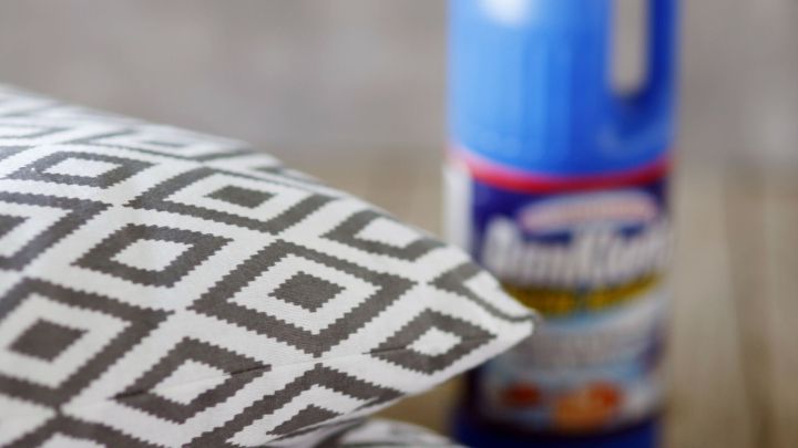 Zwei Kissen mit geometrischem Muster liegen auf einem Tisch, w&auml;hrend chlorbasierter Reiniger zur Schimmelentfernung bereitsteht.