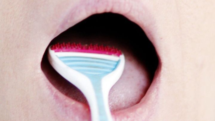 Ein Zungenschaber wird in den ge&ouml;ffneten Mund gehalten, um Mundgeruch zu bek&auml;mpfen, mit Fokus auf die Zunge.