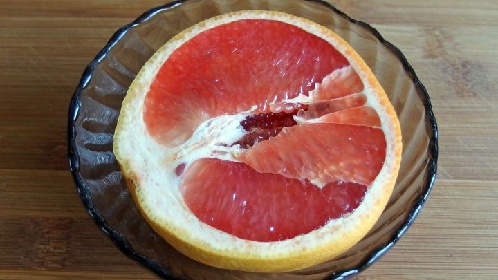 Eine Pampelmuse ist auf einem Teller auf einem Holztisch halbiert, ihre saftigen roten Segmente sind sichtbar.