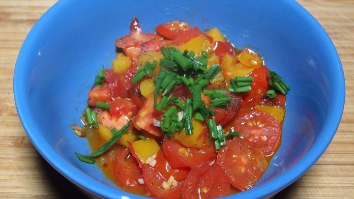 Bunte Mischung aus frischen Tomaten und Kr&auml;utern in einer blauen Sch&uuml;ssel, die als warmer Salat angerichtet ist.