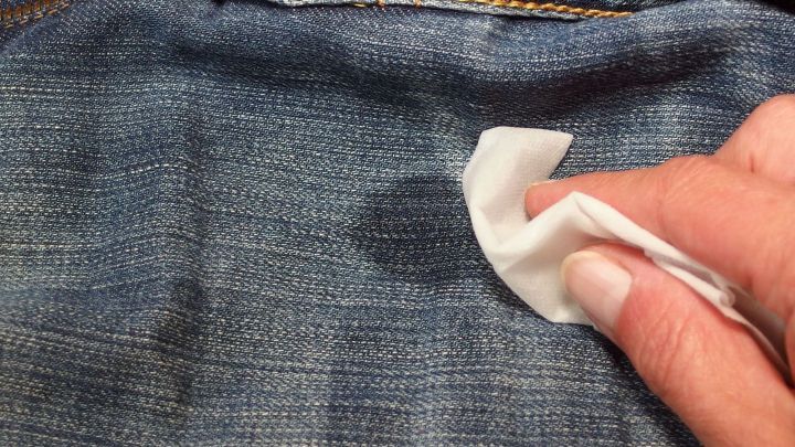 Eine Hand wischt mit einem Tuch über einen Dreckfleck auf einer Jeans, um Gras- und Dreckflecken zu entfernen.
