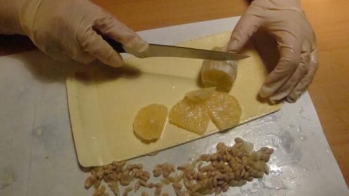 Eine Person schneidet mit einem Messer Orangenscheiben auf einem Schneidebrett, um Orangenmarmelade herzustellen.