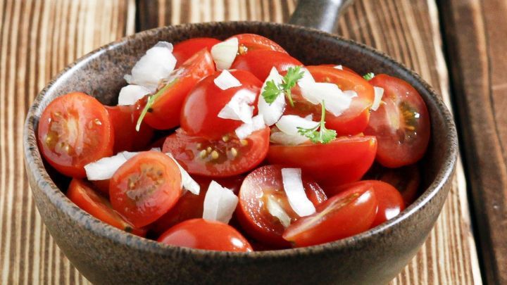 Saftige Tomaten sind in einer Sch&uuml;ssel angerichtet, mit Zwiebeln und Kr&auml;utern garniert, auf einer Holztischoberfl&auml;che.