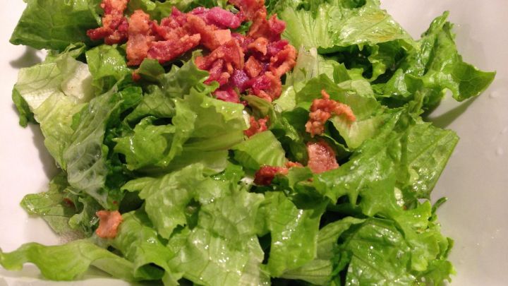 Ein gr&uuml;ner Salat mit knusprigem Speck liegt servierfertig in einer wei&szlig;en Sch&uuml;ssel.