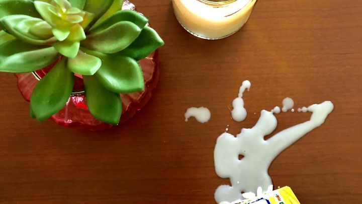 Eine Hand entfernt Wachs von einer glatten Oberfl&auml;che, w&auml;hrend daneben eine Pflanze und eine Kerze stehen.