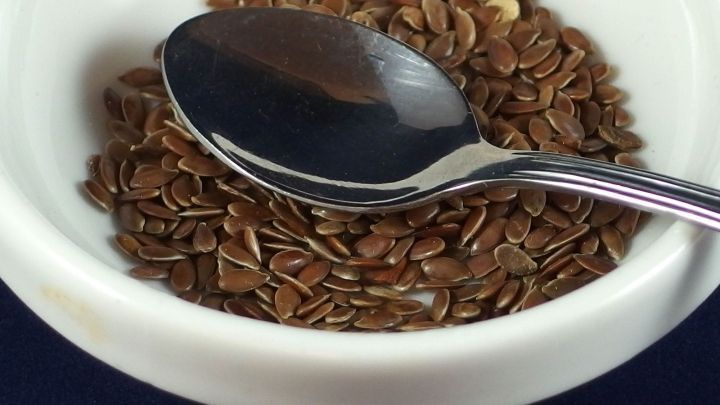 In einer wei&szlig;en Sch&uuml;ssel liegen Leinsamen, w&auml;hrend ein L&ouml;ffel daneben positioniert ist, ideal f&uuml;r eine Di&auml;t.