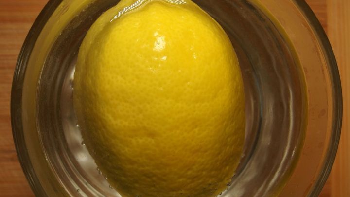 Zitrone schwimmt in klarem Wasser in einem Glas mit Holztisch als Hintergrund. Kein Text vorhanden.