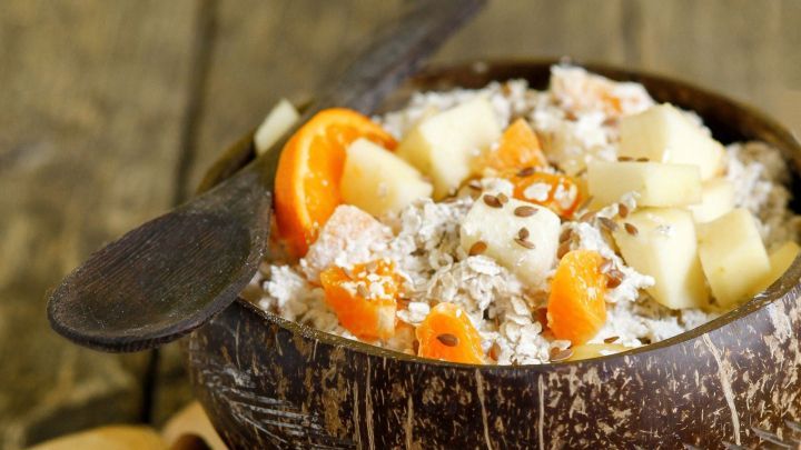 Eine mit Haferflocken, Obst und Leinsamen gef&uuml;llte Sch&uuml;ssel steht auf einem offenen Buch, umgeben von Zimtstangen.