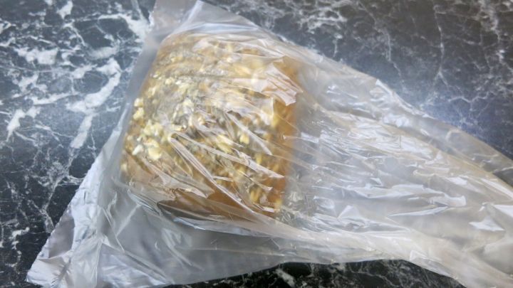 Ein altes Br&ouml;tchen liegt in Plastikfolie auf einer dunklen, marmorierten Tischoberfl&auml;che.