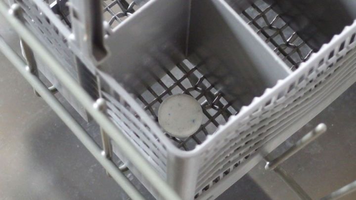Im inneren einer Sp&uuml;lmaschine liegt ein Kukident-Tab auf einem metallenen Geschirrkorb, bereit zum Reinigen.