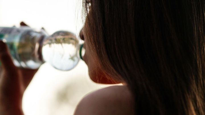 Eine Frau trinkt Wasser aus einer Flasche, w&auml;hrend sie in der Sonne steht, um Blasenentz&uuml;ndungen vorzubeugen.