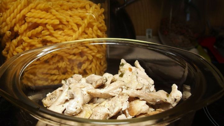 In einer Glassch&uuml;ssel liegen geschnetzelte St&uuml;cke, w&auml;hrend im Hintergrund gedrehte Nudeln sichtbar sind, bereit f&uuml;r einen Auflauf.