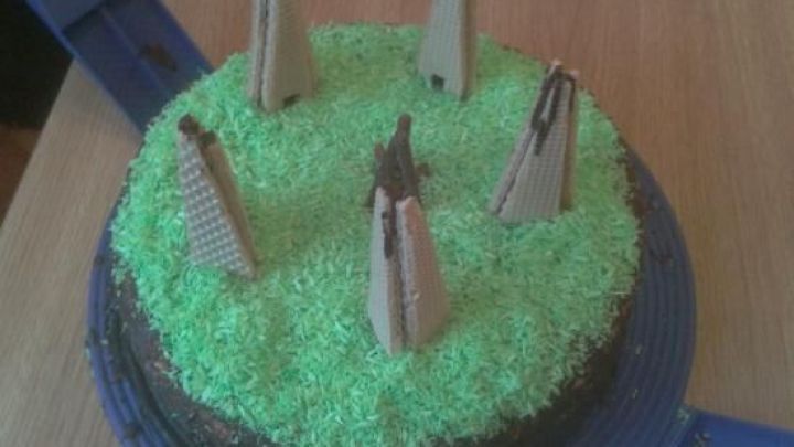 Eine Torte mit gr&uuml;ner Kokosnuss-Dekoration, die mit kleinen Schokoladenfiguren von indianischen Zelten geschm&uuml;ckt ist.