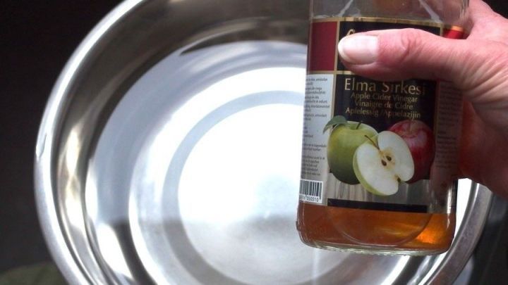 Ein Hand h&auml;lt eine Flasche Apfelessig &uuml;ber eine gl&auml;nzende Sch&uuml;ssel mit Wasser, bereit zur Mischung gegen Verstopfung bei Hunden.