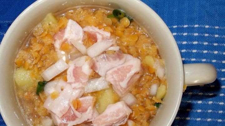 Eine Sch&uuml;ssel mit Dosensuppe liegt auf einem blauen Tisch, gef&uuml;llt mit groben Zutaten und St&uuml;ckchen von Fleisch.