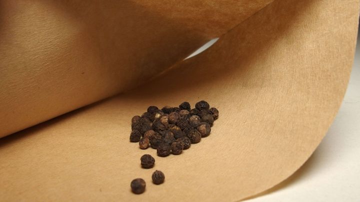 Schwarze Pfefferk&ouml;rner liegen auf einem Kaffeefilter, w&auml;hrend sie zum F&uuml;llen von Gew&uuml;rzm&uuml;hlen vorbereitet werden.