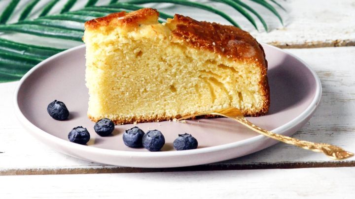 Ein saftiges St&uuml;ck Kuchen mit Apfelmus auf einem lila Teller, umgeben von Blaubeeren und gr&uuml;nen Bl&auml;ttern.
