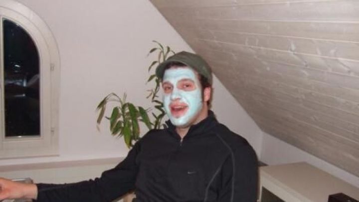 Eine Person mit Zahnpasta-Gesichtsmaske sitzt entspannt im Dachgeschoss neben einer Pflanze, vor einem Fenster.