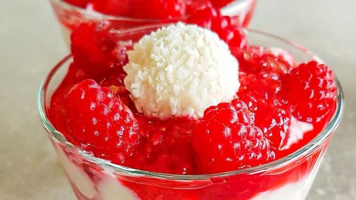 Eine transparente Schale zeigt cremige Raffaello-Creme, geschichtet mit frischen Himbeeren und einer Kokoskugel oben.