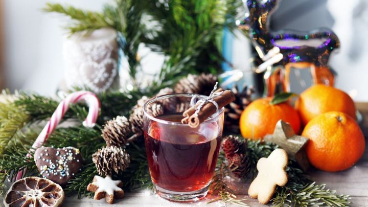 Ein Glas Chinesischer Punsch steht auf einem dekorierten Tisch, umgeben von Weihnachtsdekoration und frischen Mandarinen.