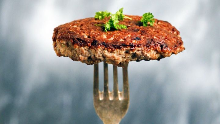 Saftige Frikadelle liegt auf einer Gabel, garniert mit gr&uuml;ner Petersilie, vor einem unscharfen, hellen Hintergrund.