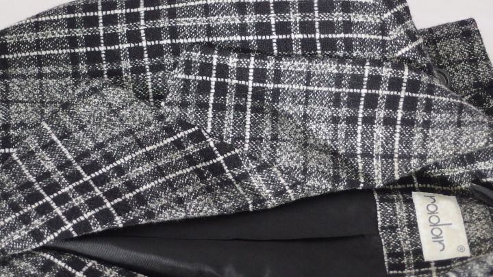 Ein kariertes Jackenrevers liegt auf einer Oberfl&auml;che und wird mit einem Gl&auml;tteisen bearbeitet, um es zu gl&auml;tten.