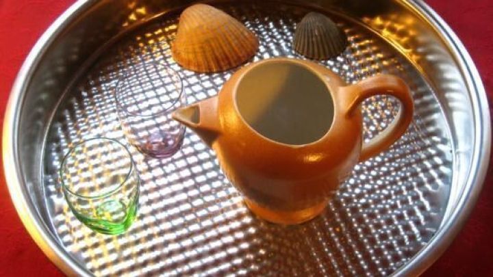 Eine metallene Backform dient als Tablett, darauf liegt eine Kanne und Muscheln, alles auf einem roten Tuch arrangiert.