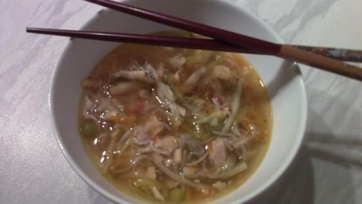 Eine Sch&uuml;ssel fern&ouml;stliche Erk&auml;ltungssuppe wird mit Essst&auml;bchen serviert, umgeben von einem schlichten, hellen Tisch.